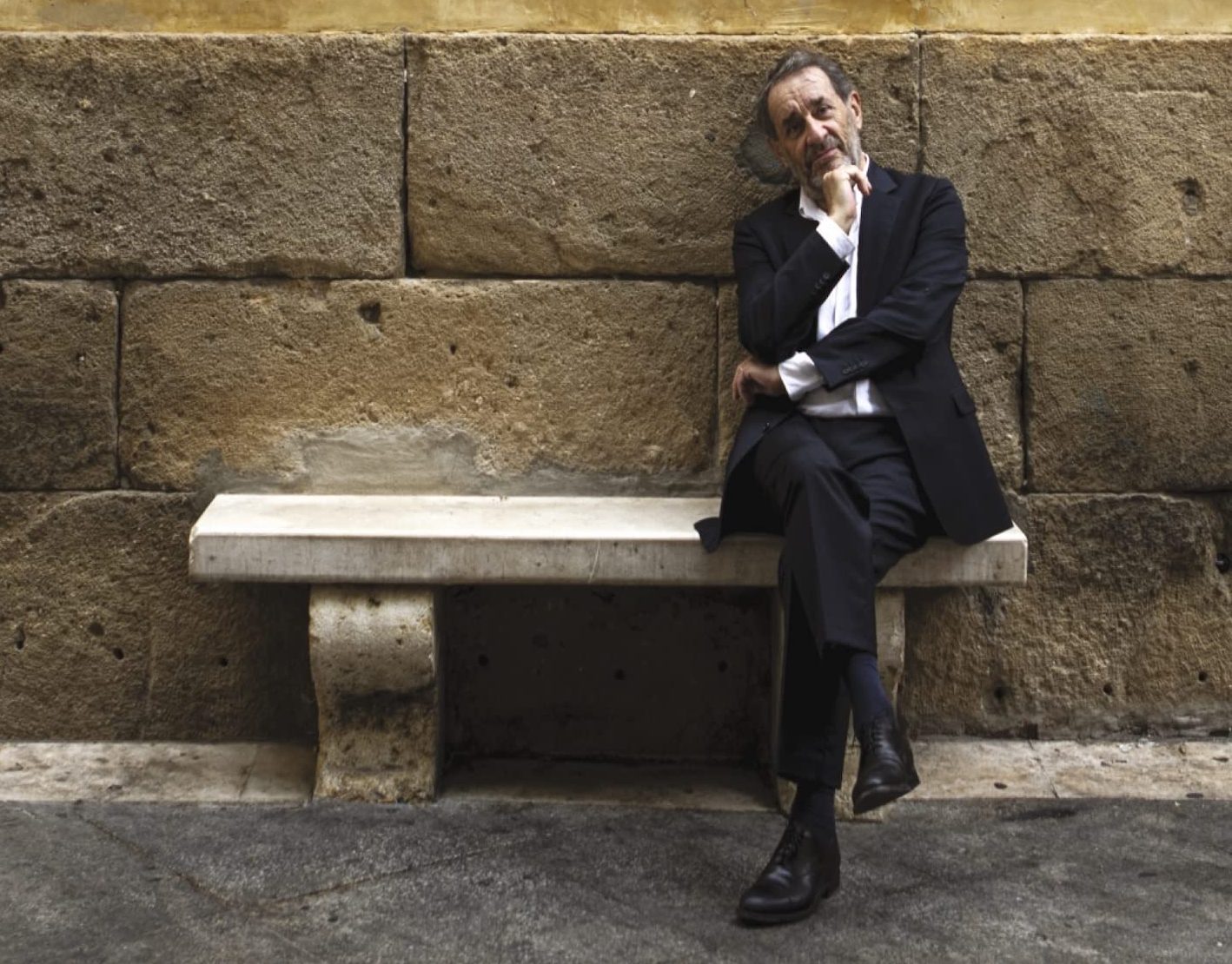 Photo représentant l'artiste Romain Didier assis sur un banc dans la rue adossé à un mur