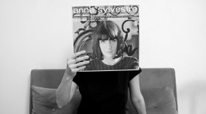 Photo en noir et blanc représentant une jeune femme assise avec une pochette de disque d'Anne Sylvestre devant le visage