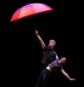 Photo représentant une femme et un homme en train de danser avec un parapluie rouge ouvert.
