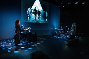 Photo représentant un musicien tourné vers un écran de cinéma en train de jouer de la musique pour accompagner le film projeté