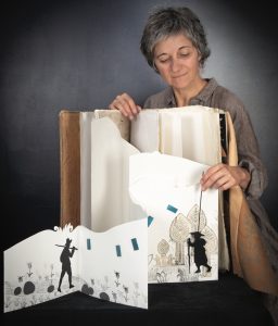 Photo représentant une artiste tenant un grand livre en papier découpé.