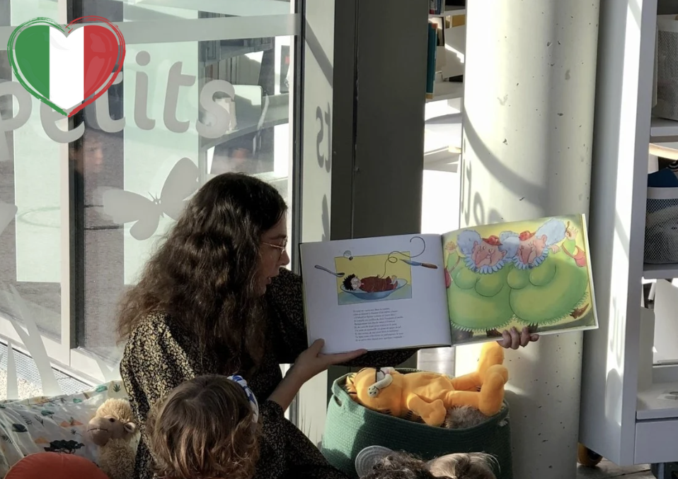 ptites oreilles Photo représentant une jeune fille en train de lire un album pour enfants. À gauche, on distingue le drapeau de l'italie