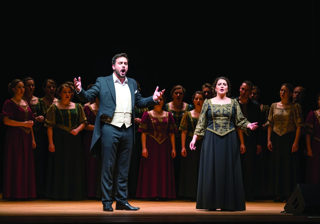 Photo représentant un chanteur d'opéra à gauche vêtu d'un smoking et une chanteuse d'opéra vêtu d'une robe.