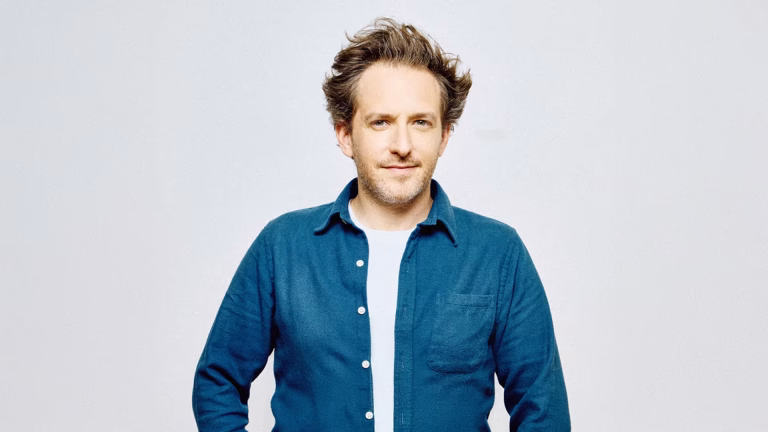 Photo représentant un jeune homme brun portant une chemise en jean et un tee-shirt blanc. Il regarde fixement l'objectif.