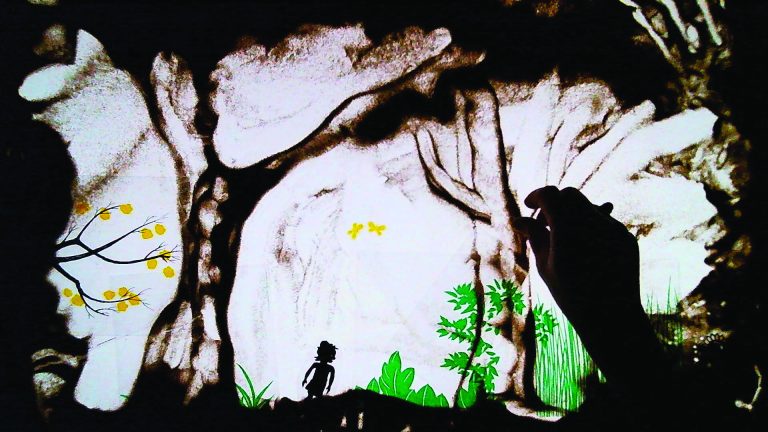 Photo représentant une main sur une table lumineuse en train de dessiner dans le sable.