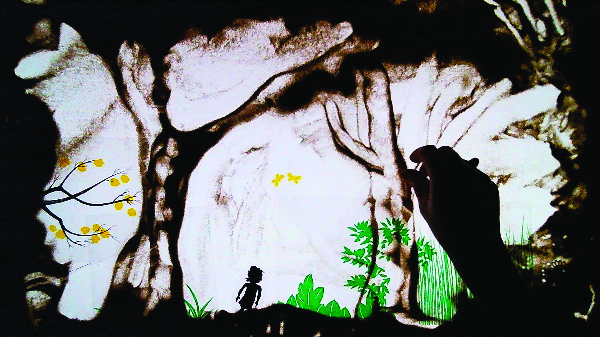 Photo représentant une main sur une table lumineuse en train de dessiner dans le sable.