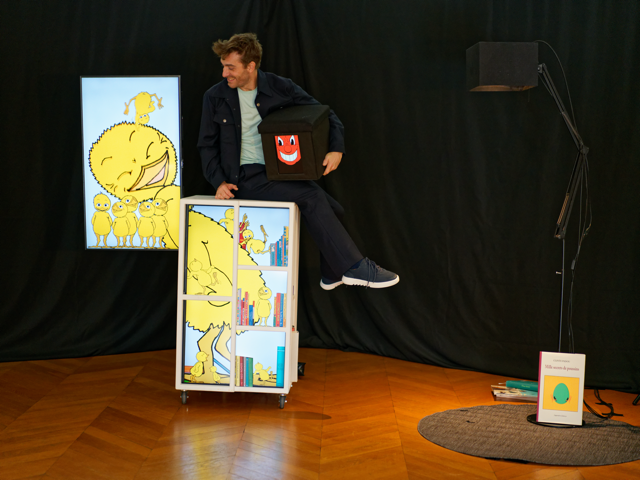 Photo représentant un comédien sur scène en train d'observer un poussin dans un écran