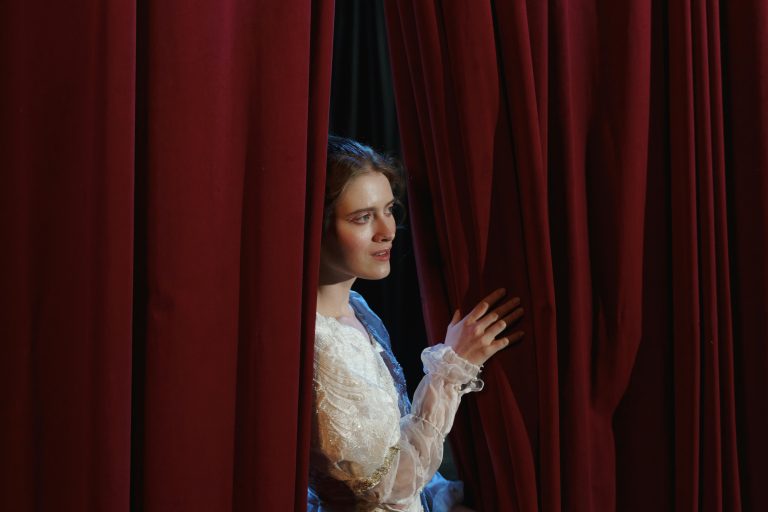 Photo représentant une jeune femme, en coulisses, cachée derrière le rideau d'un théâtre