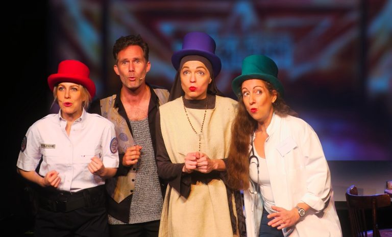 Photo représentant un groupe, trois chanteuses et un chanteur. ils portent des chapeaux haut de forme et son en train de chanter sur scène n grimaçant.
