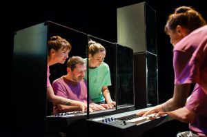 Photo représentant 3 musiciens au piano, deux femmes et un homme. Les deux femmes sont vêtues de tee-shirt rose et l'homme d'un tee-shirt vert.