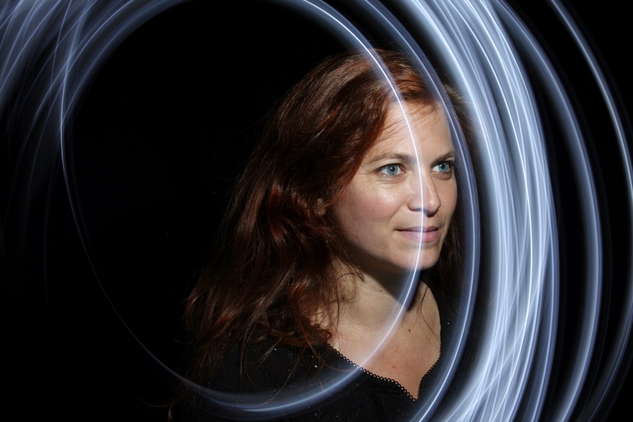 Photo représentant une jeune femme au regard perçant en train de fixer l'objectif. Il y a demi-cercle lumineux blanc qui traverse la photo