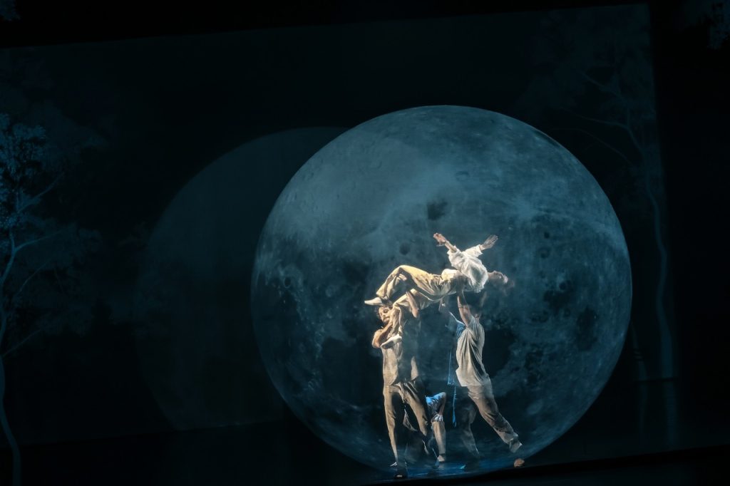 Photo représentant 3 danseurs sur un fond de lune. Une des danseuse est portée par les deux autres.