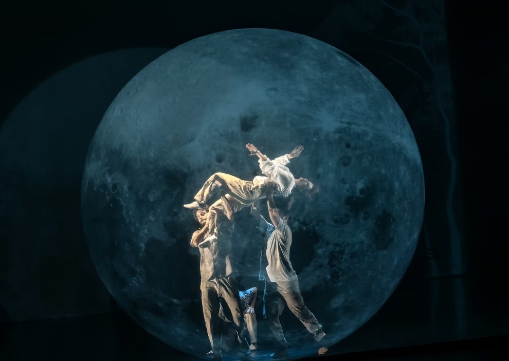 Photo représentant 3 danseurs sur un fond de lune. Une des danseuse est portée par les deux autres.