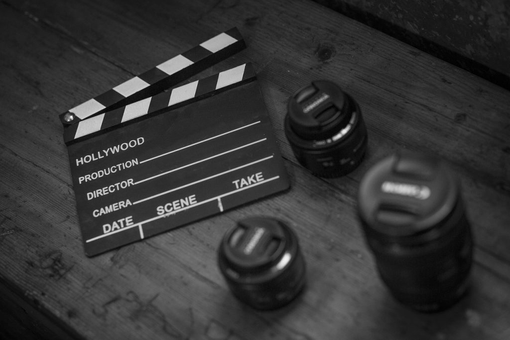 Photo représentant un clap de cinéma posé une table en bois noir. Il est entouré d'objectifs d'appareils photos.