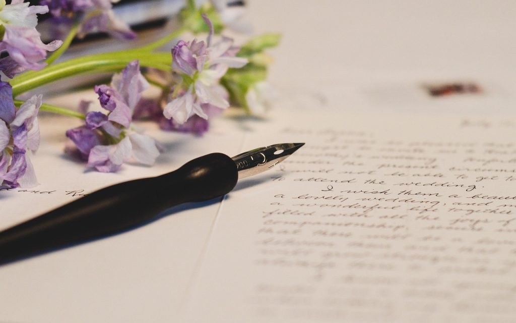 Photo représentant une feuille de papier avec une écriture manuscrite. Dessus on y voit un stylo plume et un bouquet de fleurs violettes