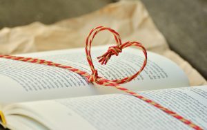 Photo représentant un livre ouvert avec un coeur tissé avec des ficelles rouges et jaunes.
